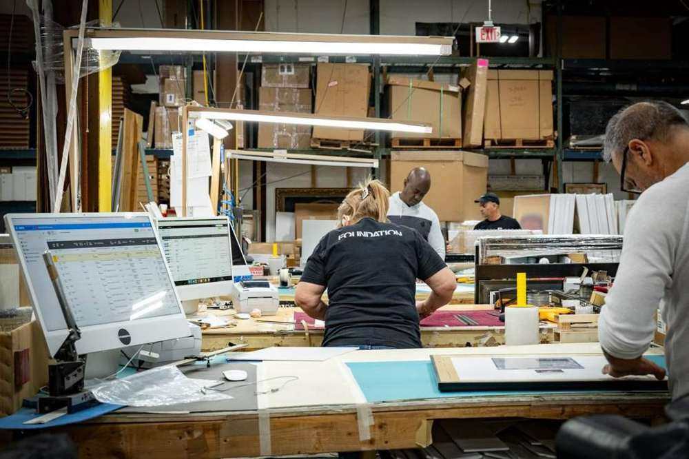 Foundation production crew packing and coordinating framed work beside warehouse racks of shipping cartons