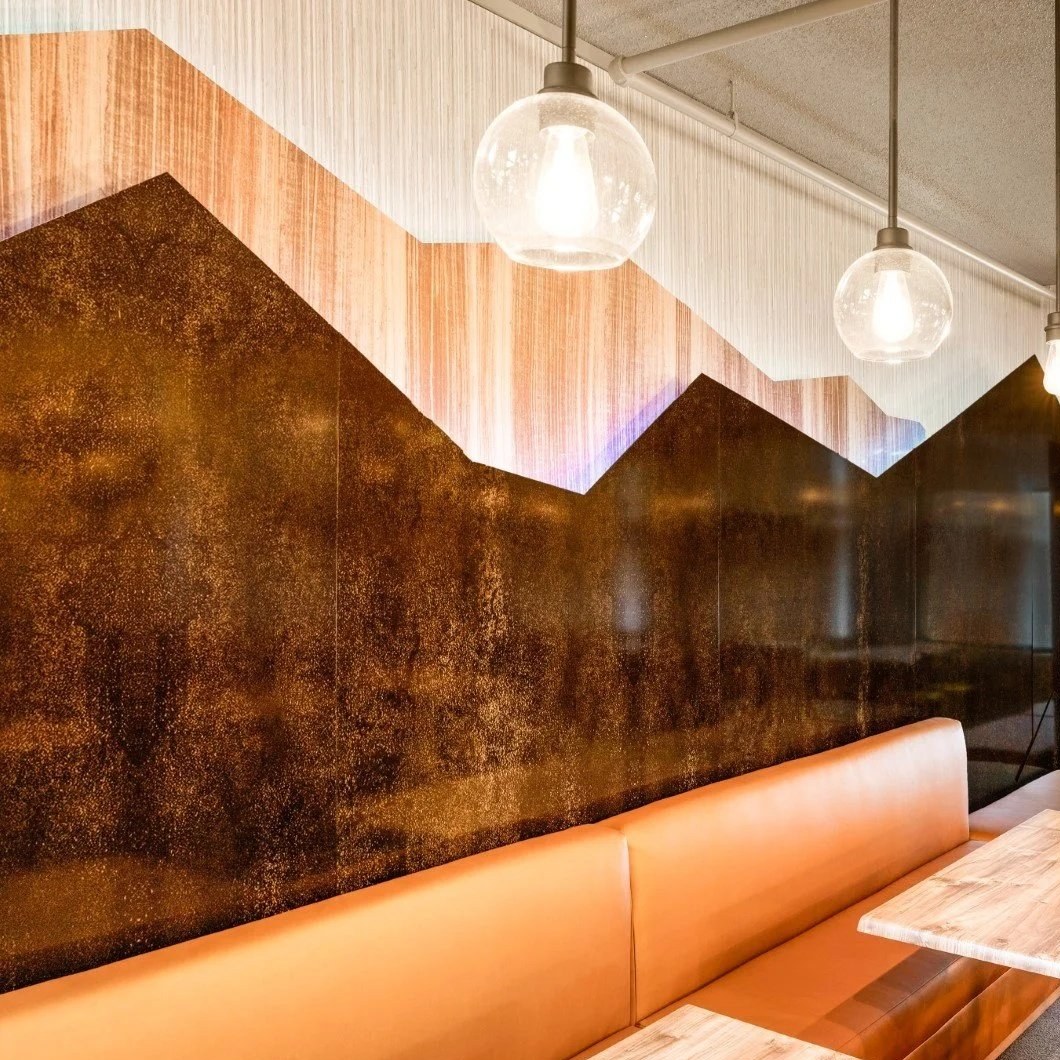Wood-plank and rusted-metal mountain silhouette feature wall above an orange banquette at Massanutten Resort